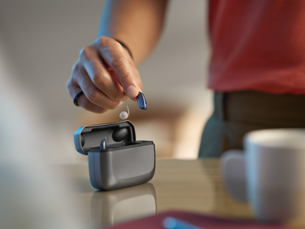 Patient placing a hearing aid in its case after professional hearing aid cleaning at Better Hearing Clinic in McAllen, TX