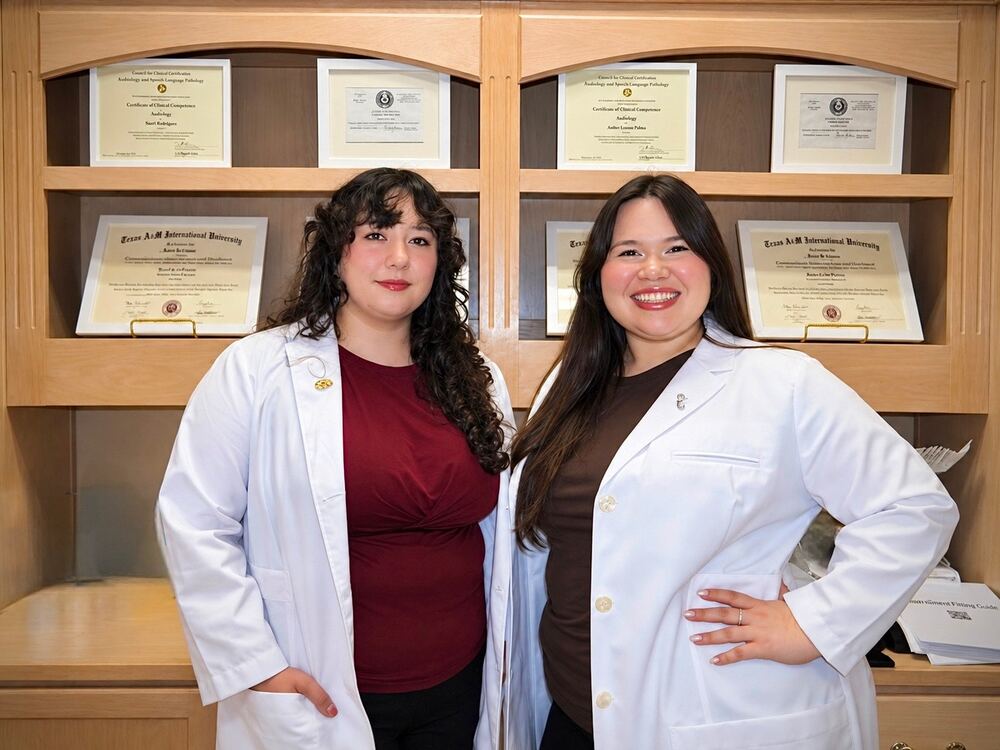 Two Doctors of Audiology in white coats in front of their diplomas at Better Hearing Clinic in McAllen, TX